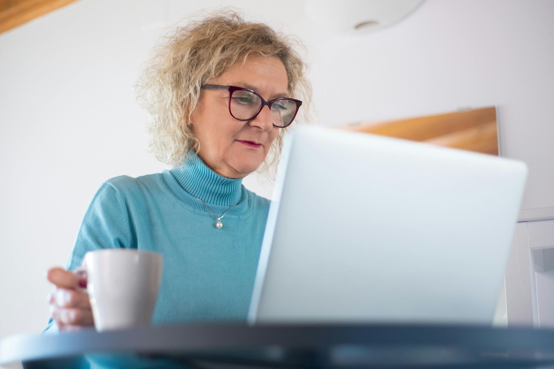 Person using a laptop while holding a white mug in a bright room