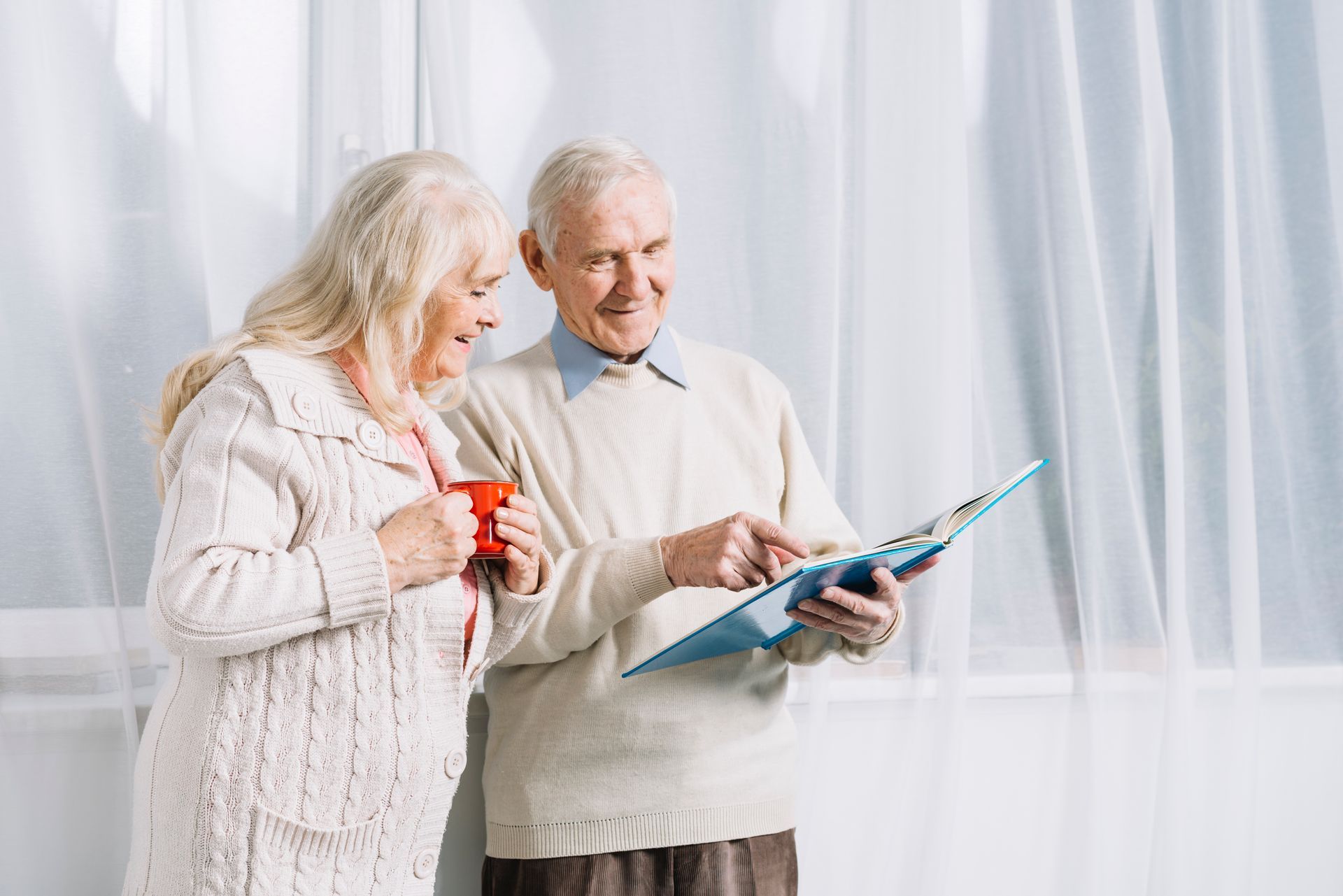 Two elderly people looking at a blue book together by a bright window