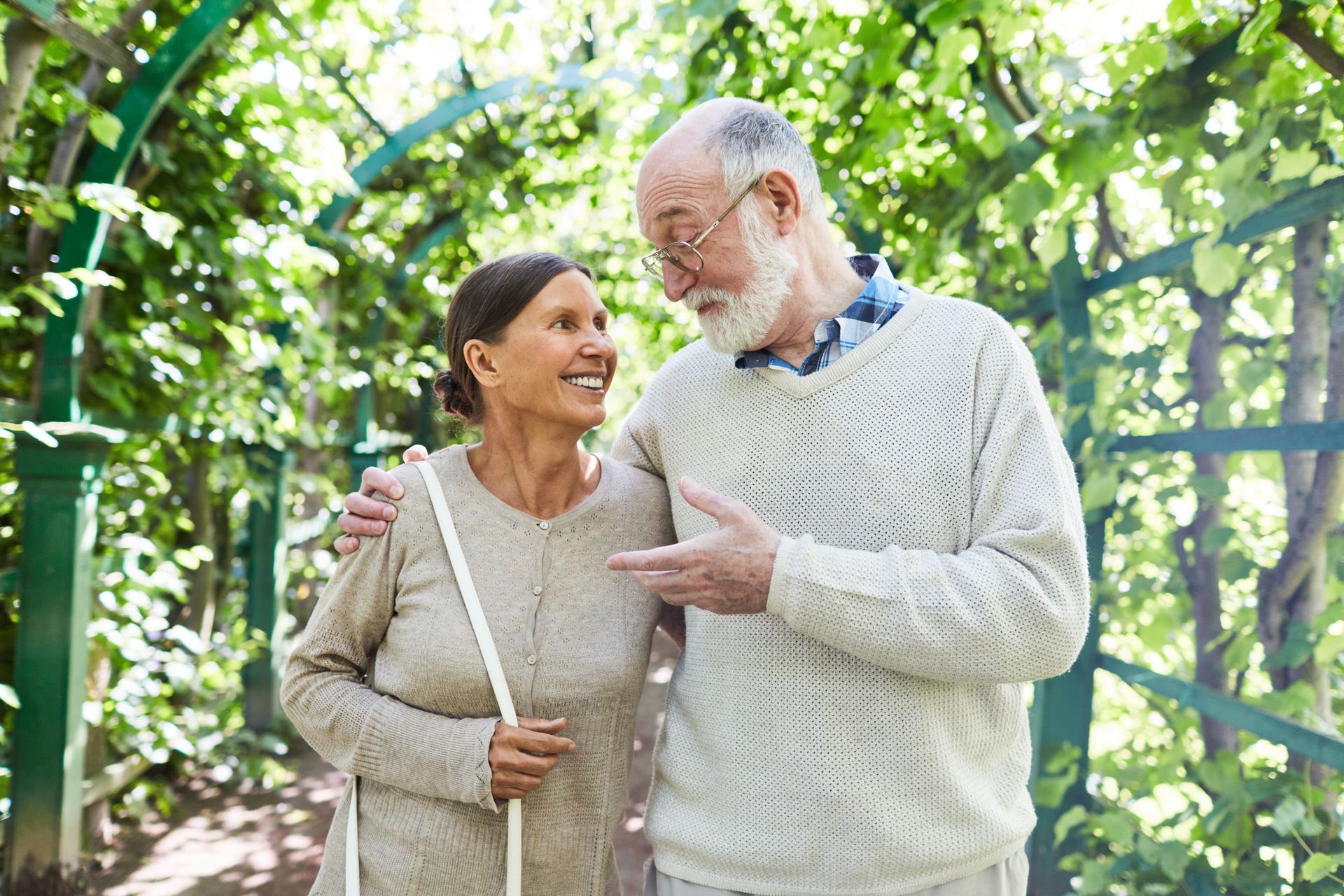 Smiling couple in sweaters walking together in a sunny garden with green vines