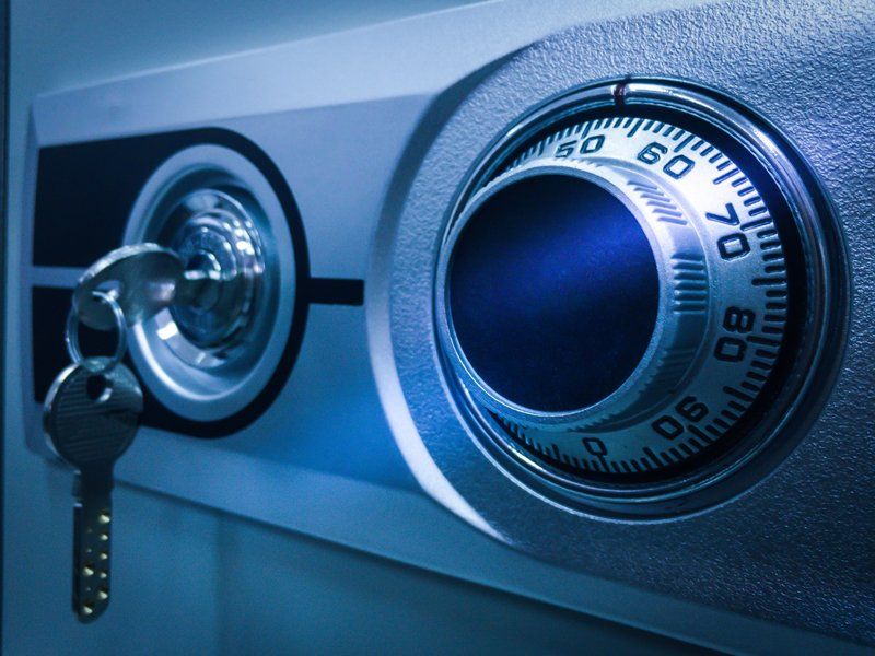 A close-up of a metal safe door with a key inserted in the lock next to a circular combination dial.