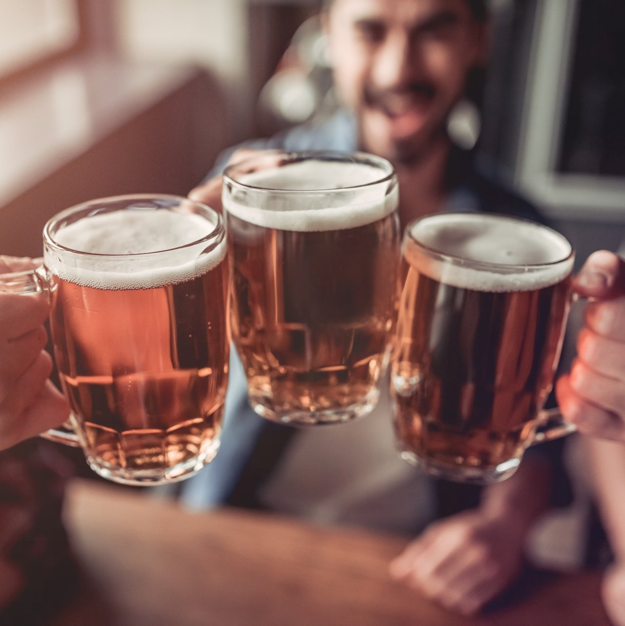 A group of people are toasting with three mugs of beer.