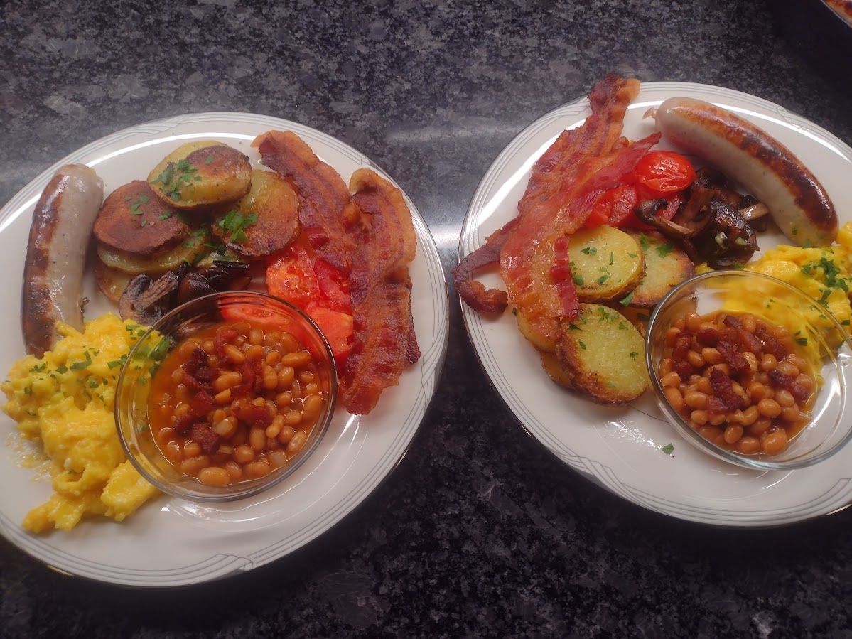 Two plates of food with bacon , eggs , beans , potatoes and sausage on a table.