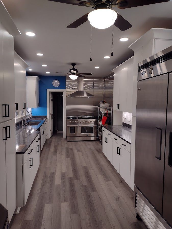 A long kitchen with stainless steel appliances and a ceiling fan.