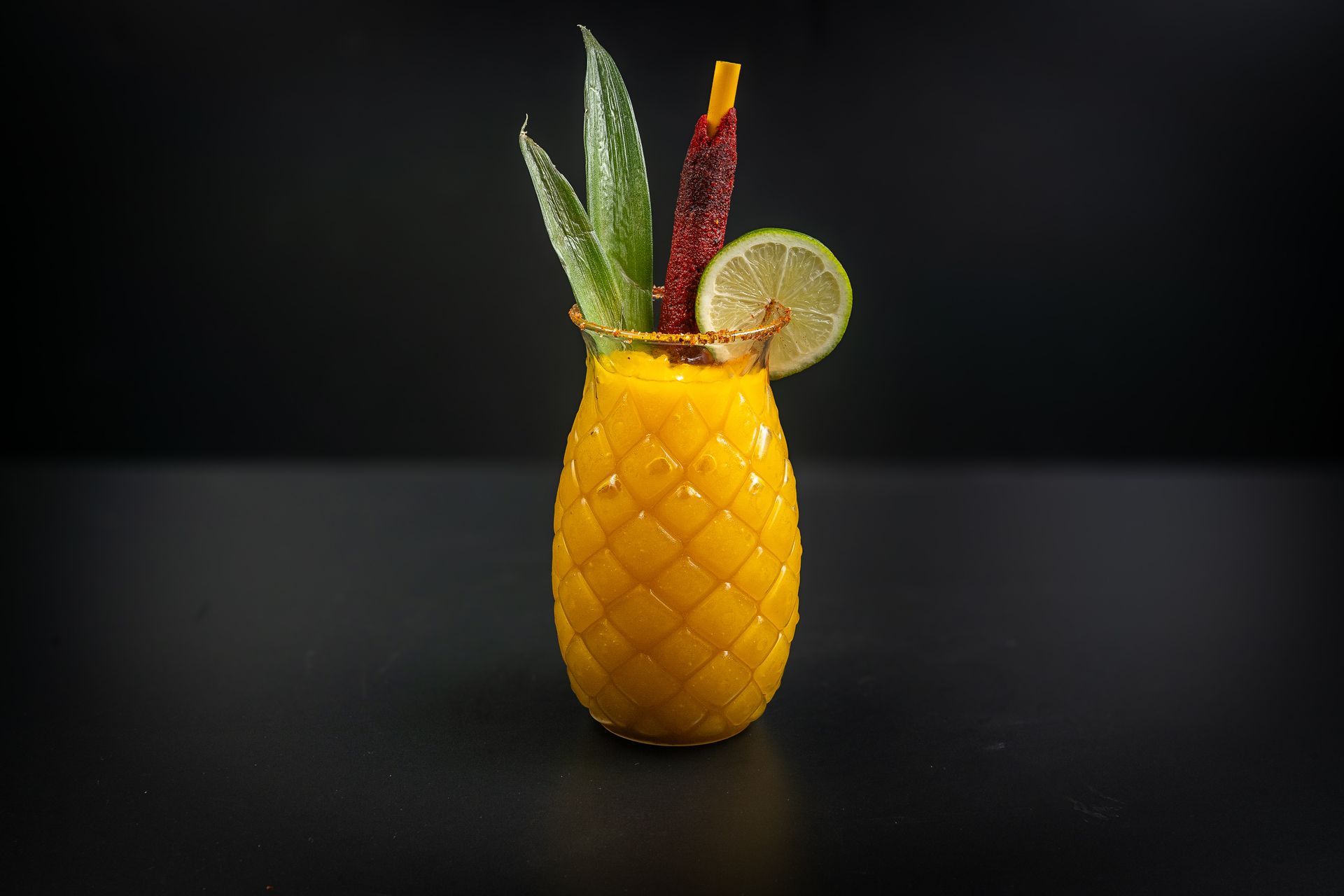 Pineapple-shaped cocktail with mint, citrus slice, and red garnish on a dark background