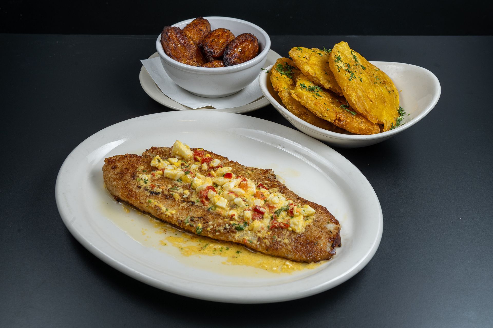 Plate of grilled chicken with side bowls of sweet plantains and tostones