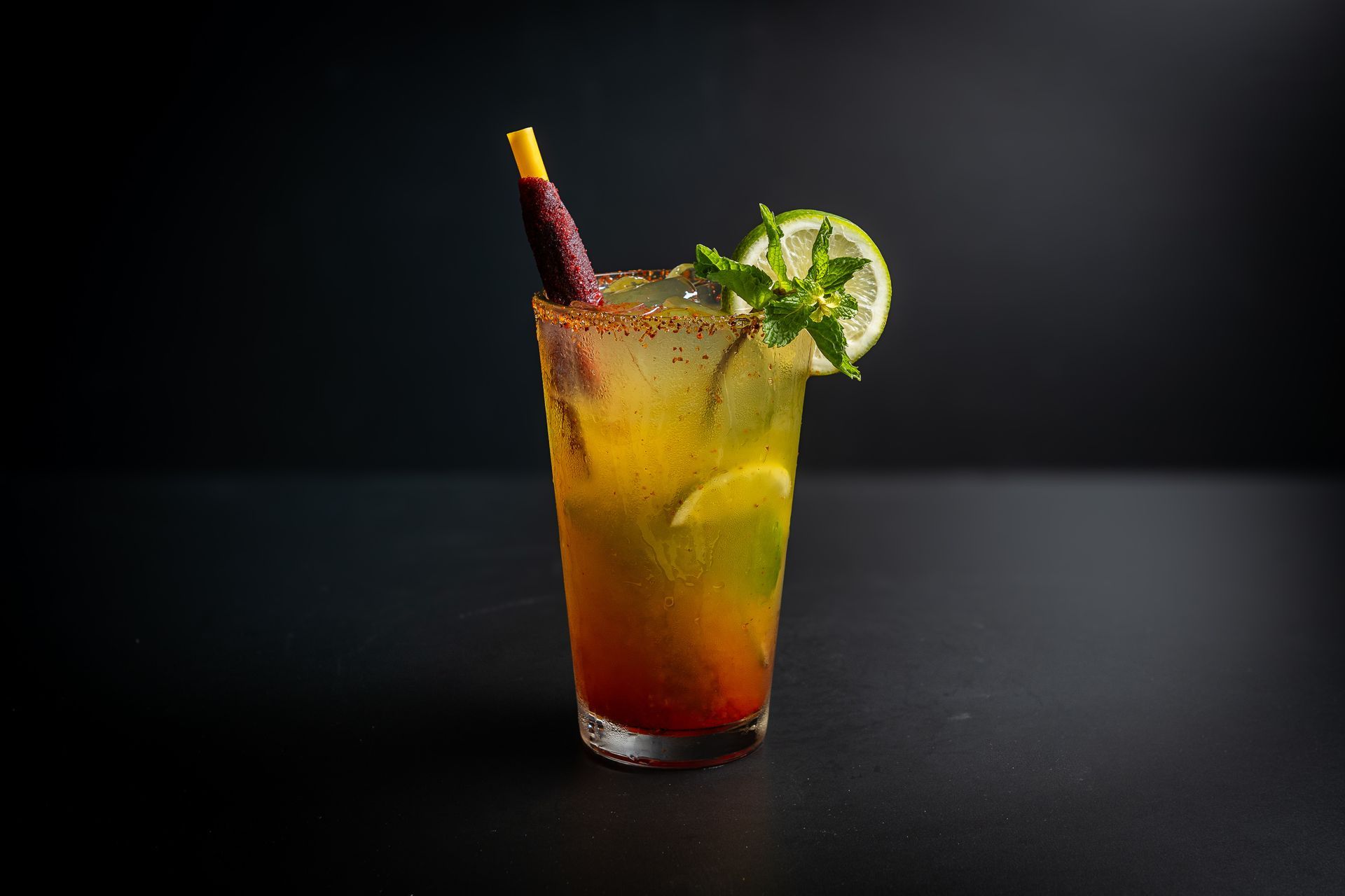 Tall layered cocktail with a lime slice and straw on a dark background