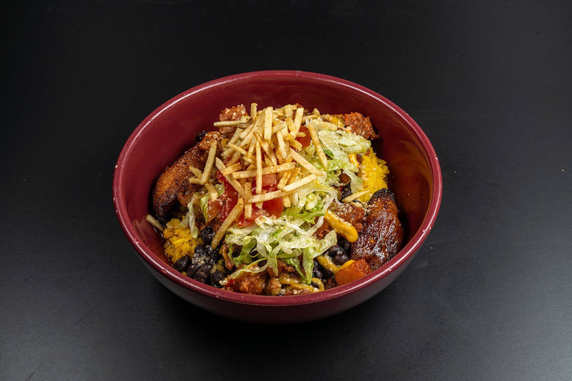 Bowl of yellow rice filled with plantain and black beans with salad and tortilla strips on top