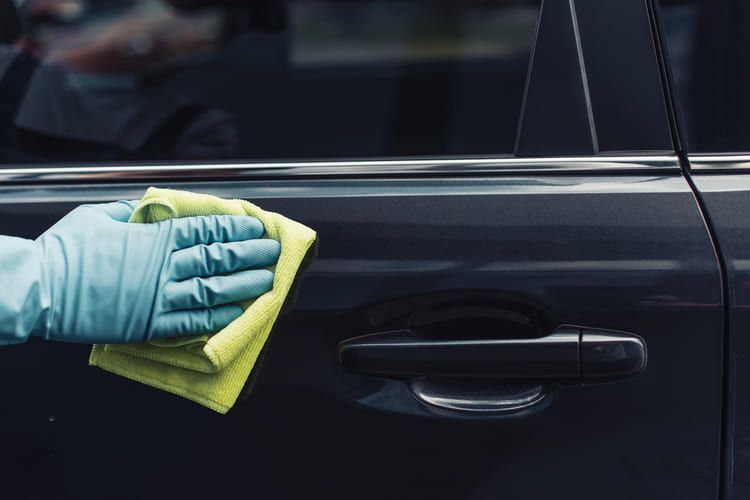 A person is cleaning a car with a cloth and gloves.