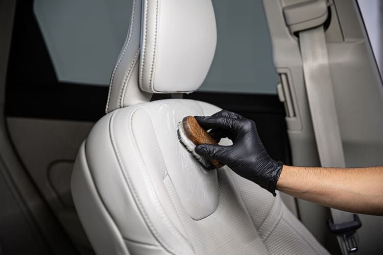 A person is cleaning a car seat with a brush.