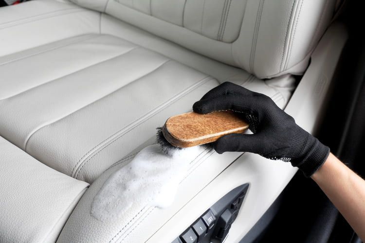 A professional cleaning a car seat with a foam formula and a brush.
