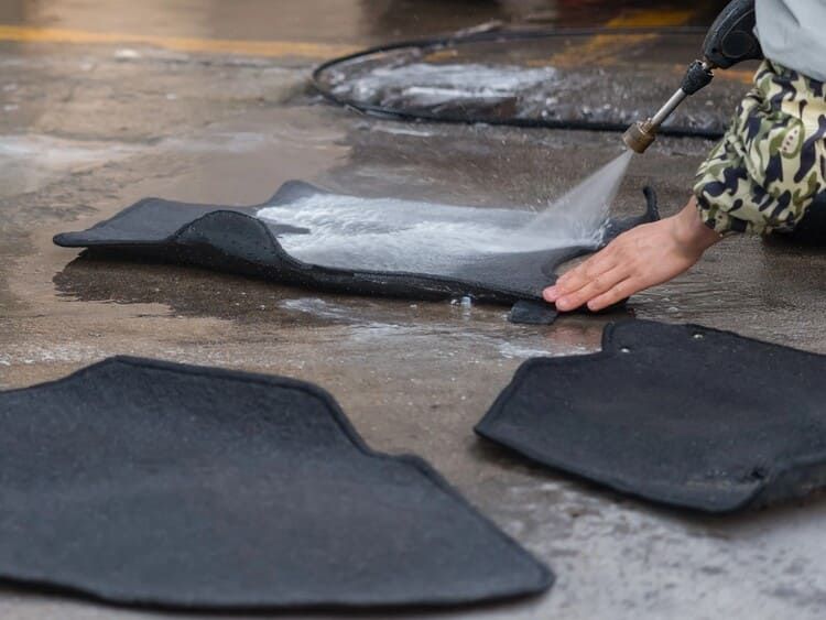 A person is cleaning a car mat with a high pressure washer.