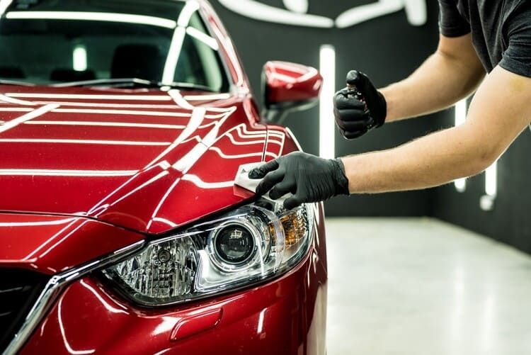 A man is polishing the headlight of a red car with a clay bar.
