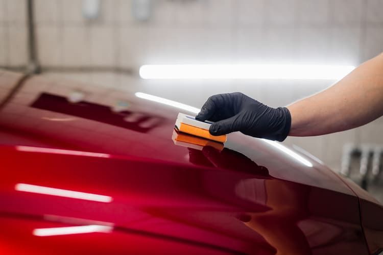 A person is polishing the hood of a red car with a ceramic coating applied.
