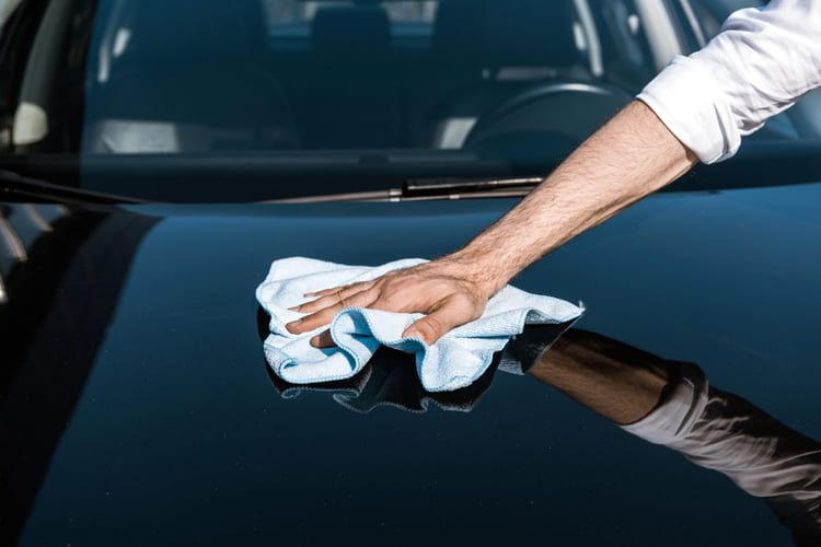 Man cleaning black car with while cloth