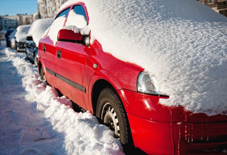 A red car covered in snow, parked on the side of the road