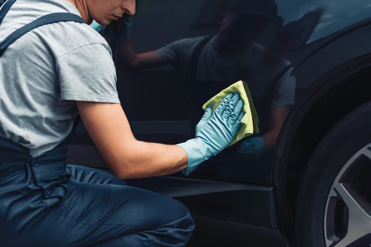 A man is cleaning a car exterior with a cloth.
