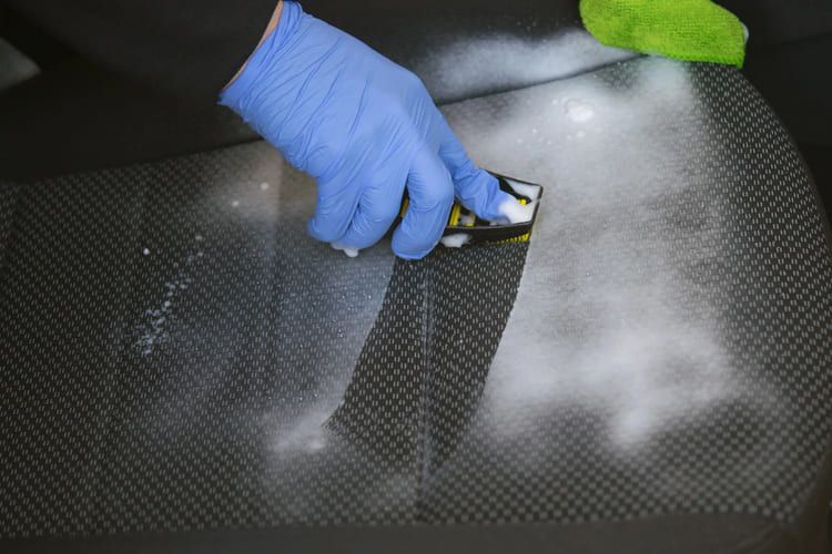 A professional wearing blue gloves and removing car seat stains with a sponge.