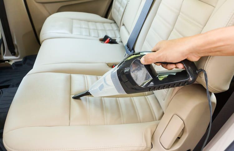 Car interior back seat vacuuming for dirt or debris removal.
