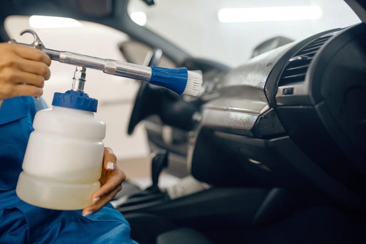 A professional worker cleaning the interior of a car with a spray bottle.