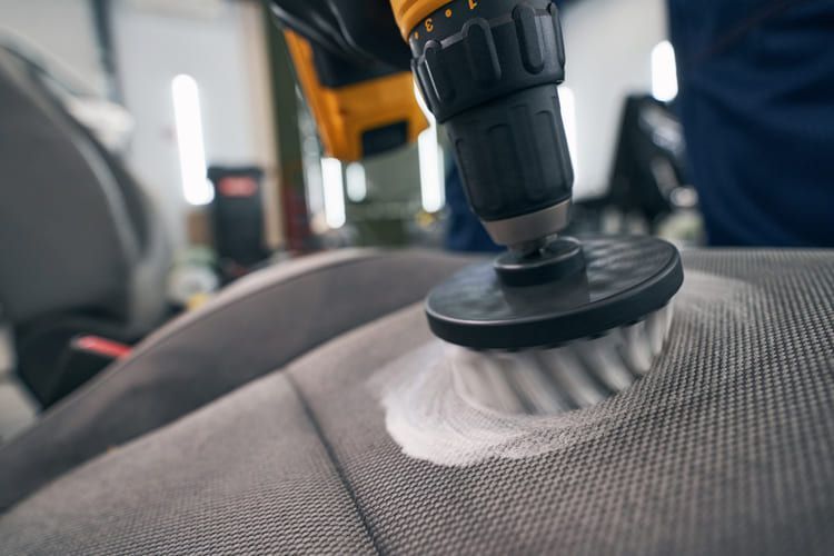 A person is cleaning a car seat with an automatic wash brush.