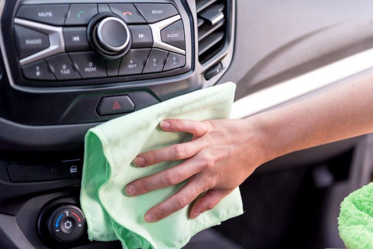 A person is cleaning the dashboard of a car with a microfibre cloth.