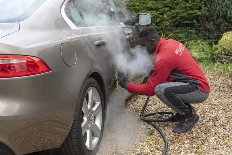 A man is cleaning a car with steam.
