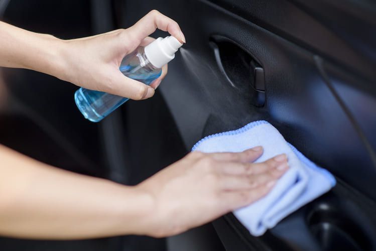 A person is cleaning a car door with an odour removal spray and a cloth.
