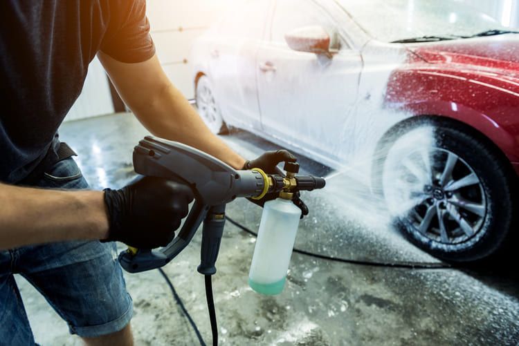 A man is washing a red car with a high pressure washer.