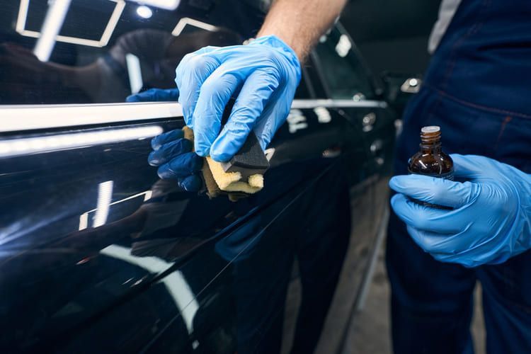 A man wearing blue gloves is applying a layer of ceramic coating.