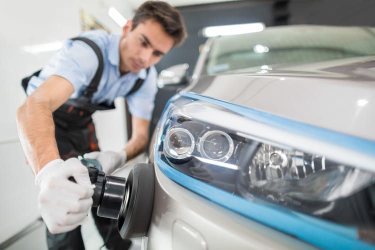 A man is polishing the headlights of a car.