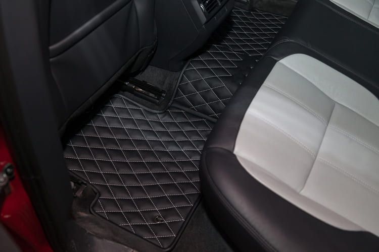 The back seat of a car with a black and white quilted protective floor mat.