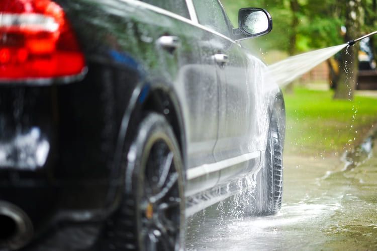 A car is being washed by its owner with a high-pressure washer.