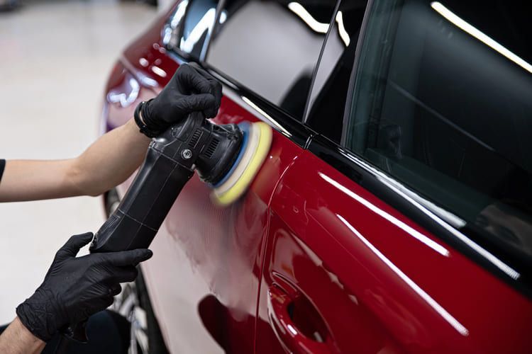 A person is polishing the hood of a car with an air sander.