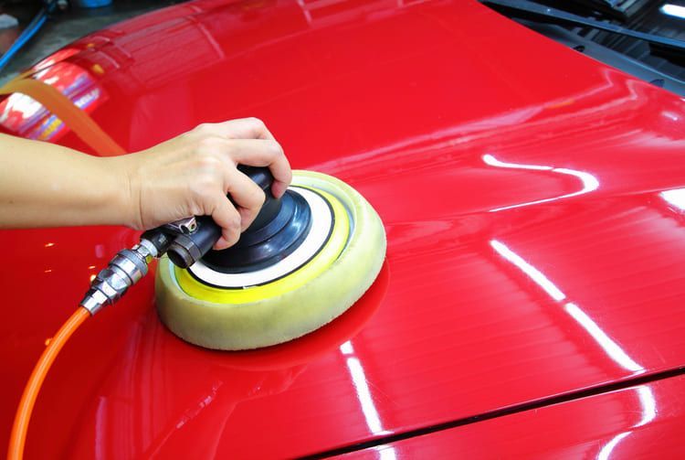 A professional is traditionally waxing a car exterior.
