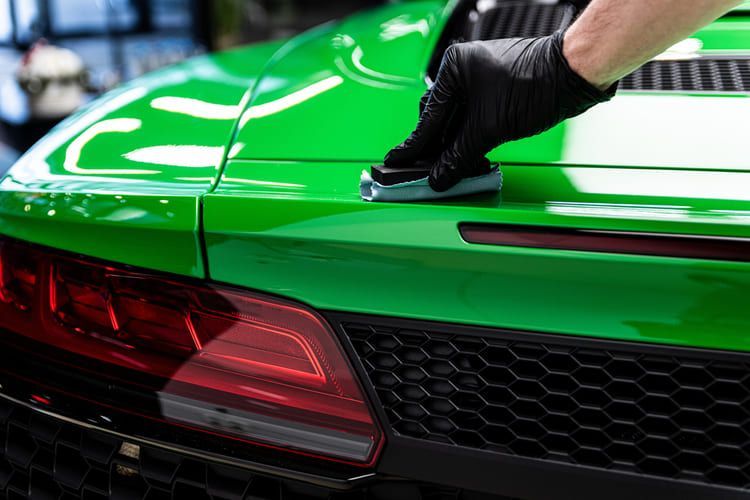 A person is applying ceramic coating onto the hood of a polished car