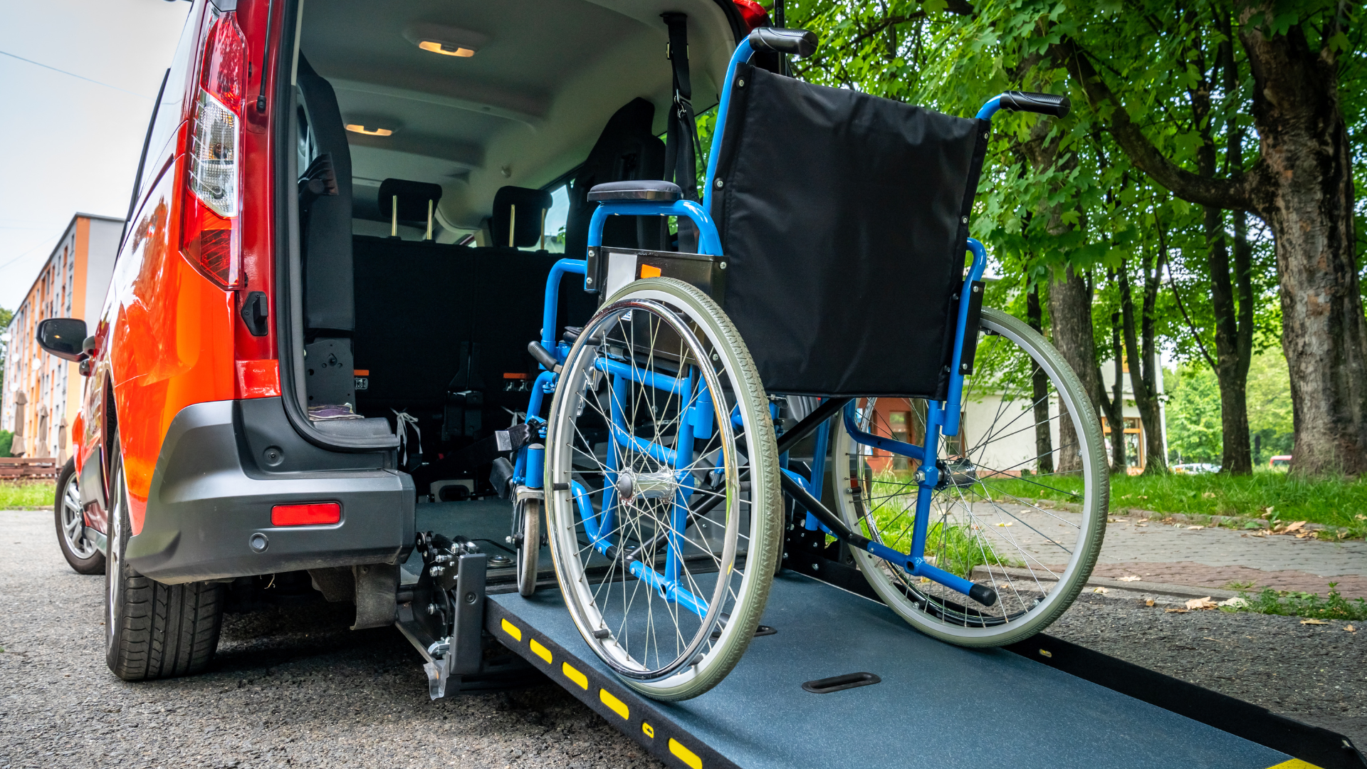 Wheelchair on a van lift, with the rear doors open and a ramp extended outdoors.