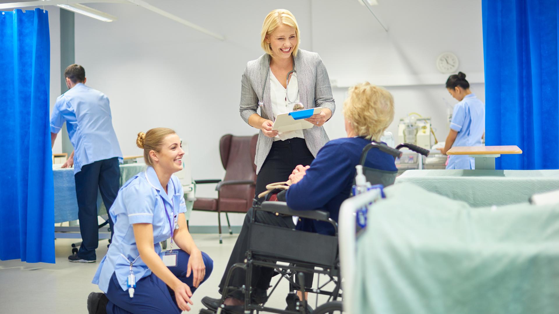 Hospital staff assisting a patient in a wheelchair near a bed in a bright medical room