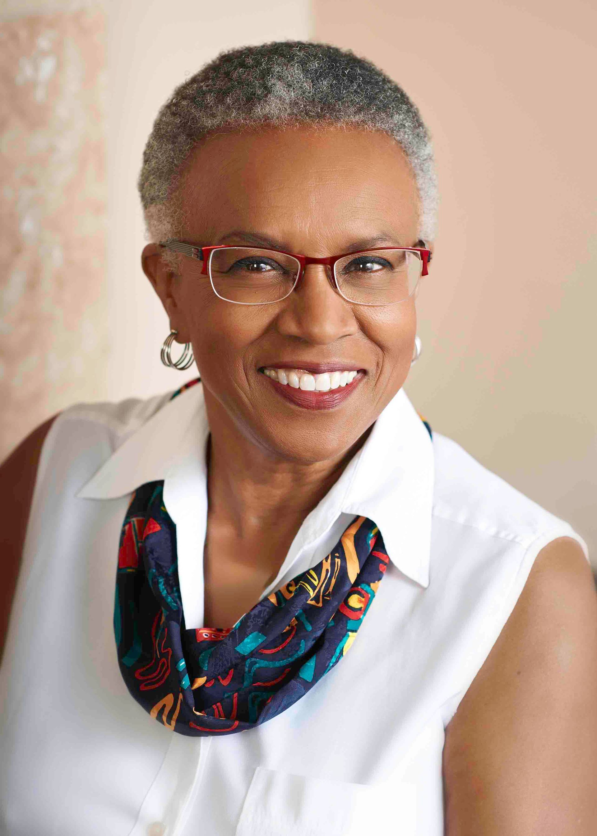 Woman with short grey hair wearing glasses and a colorful scarf, smiling.