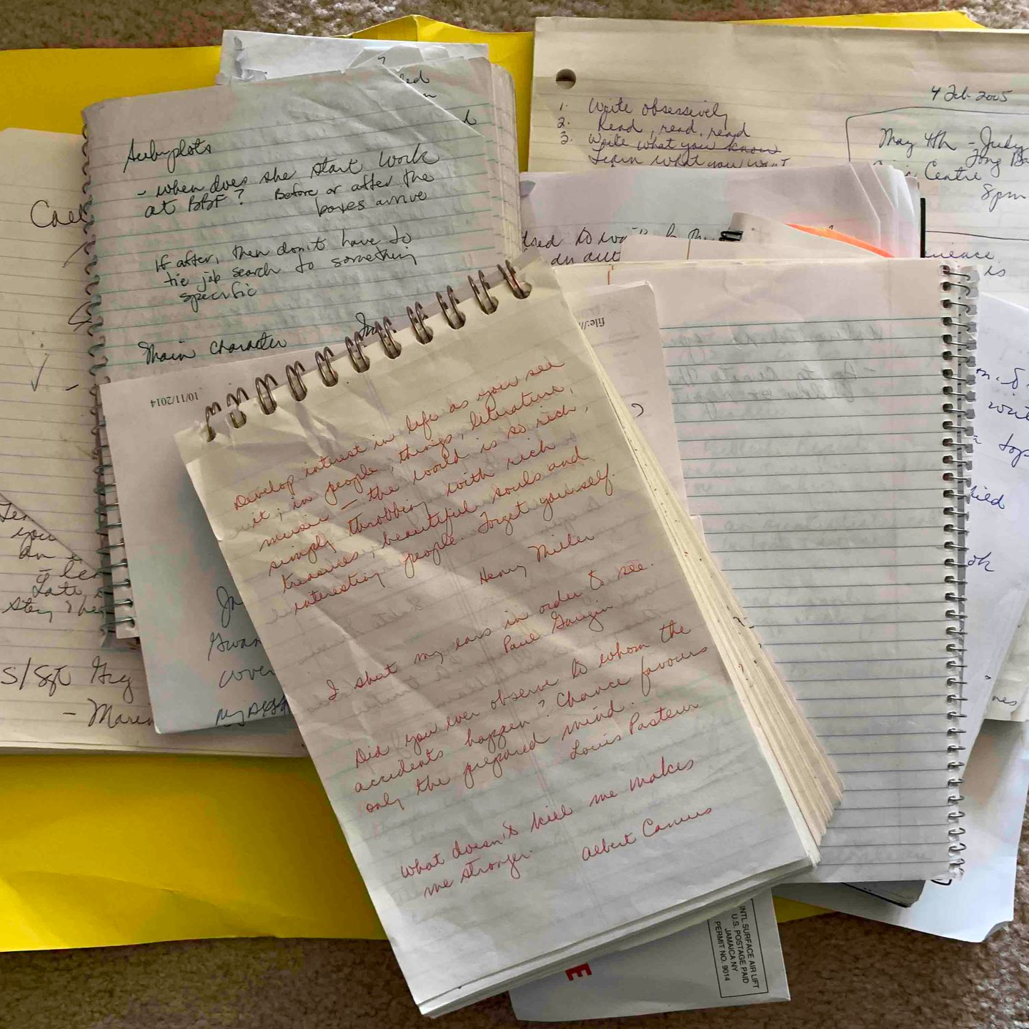 Pile of handwritten notes and notebooks on a yellow surface.