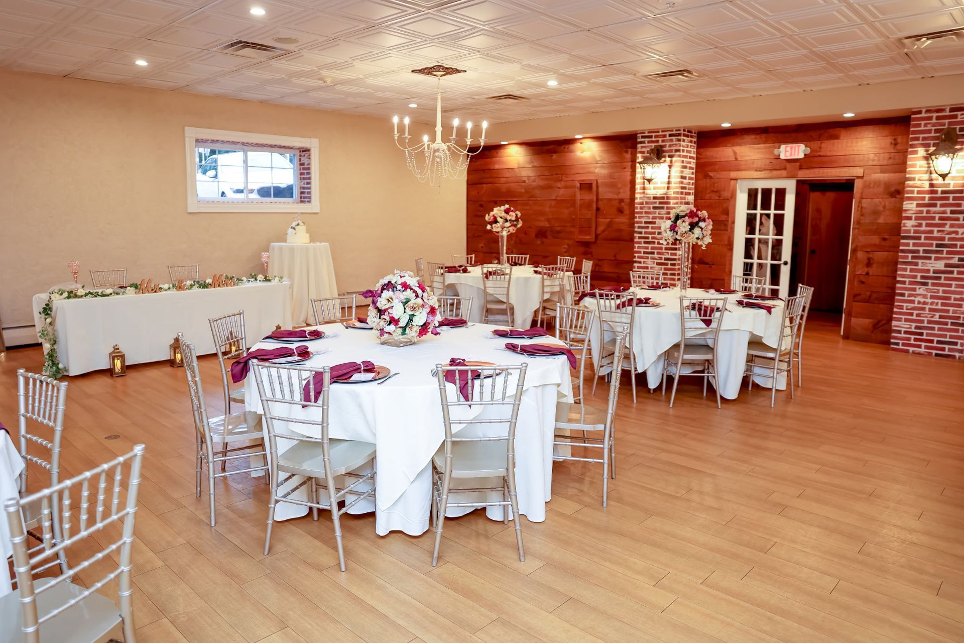 Banquet hall with round tables set for a formal event; gold chairs, white linens, floral centerpieces.