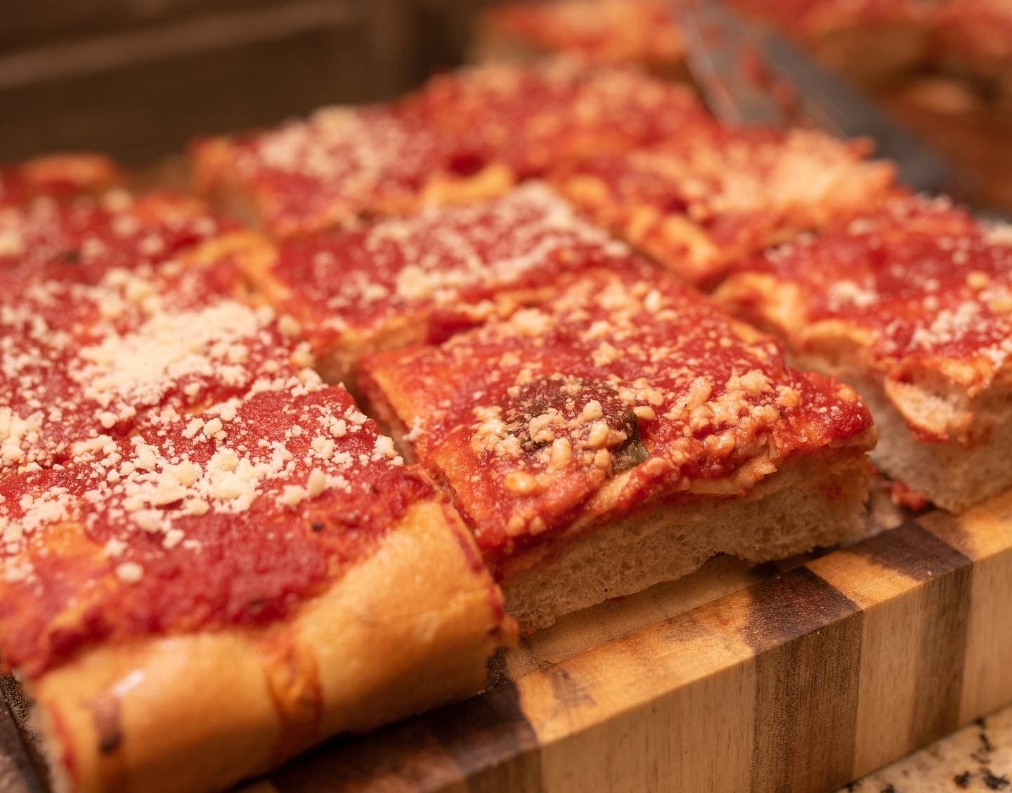 Square-cut pizza with red sauce and sprinkled cheese on a wooden cutting board.