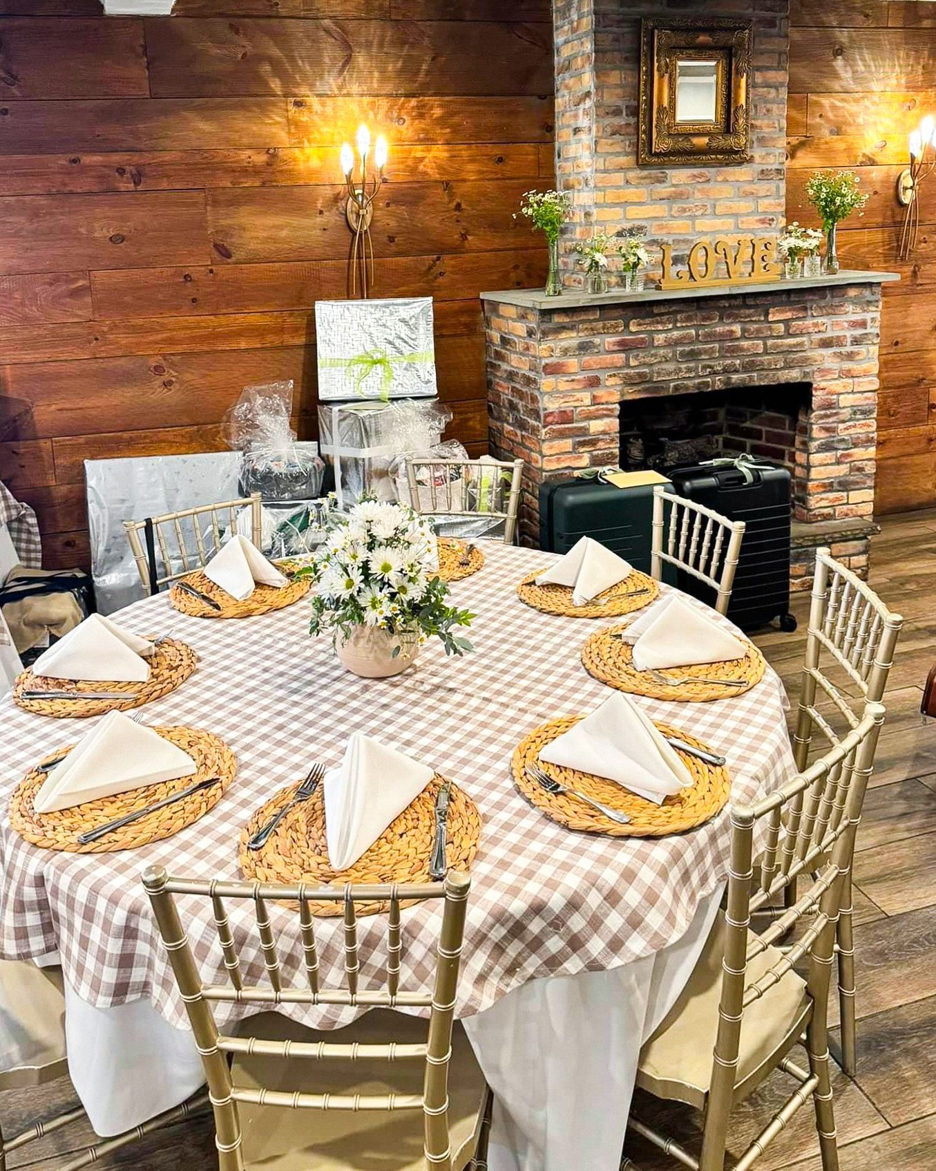 Round tables set for a gathering, with pink napkins and floral centerpieces, in a room with a fireplace.