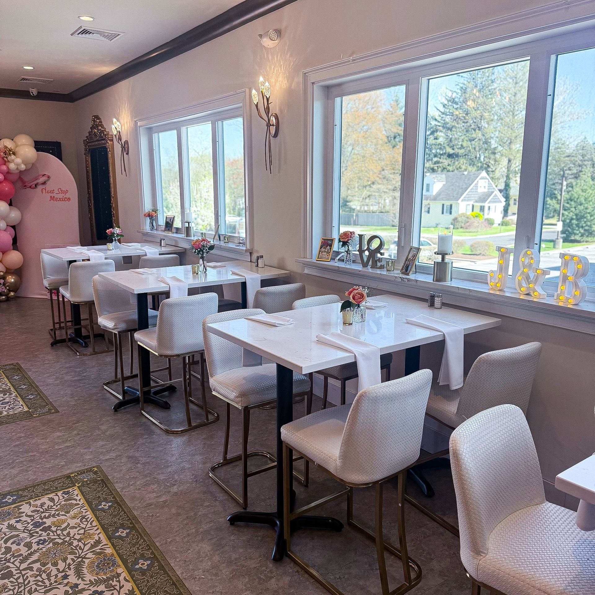 Interior of a bar/restaurant with chandelier lights, teal bar, and white tables and chairs.