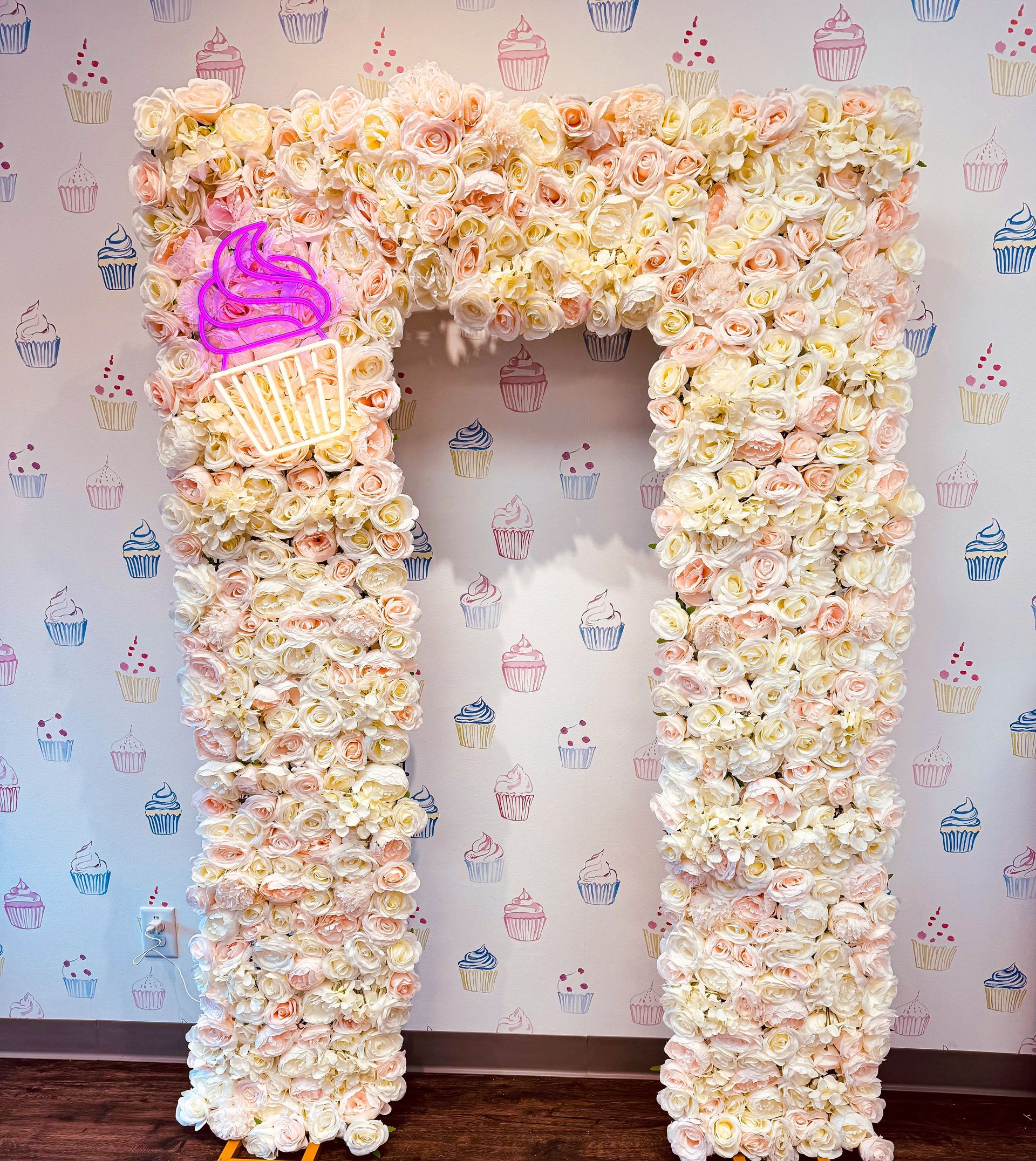 White floral archway with a pink accent, set against patterned wallpaper.