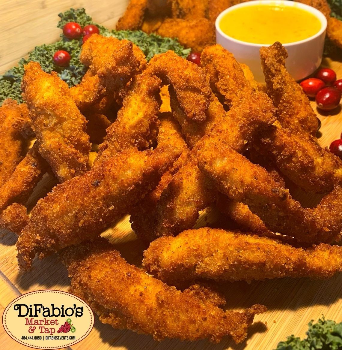 Crispy breaded chicken wings with dipping sauce and red berries on a serving platter