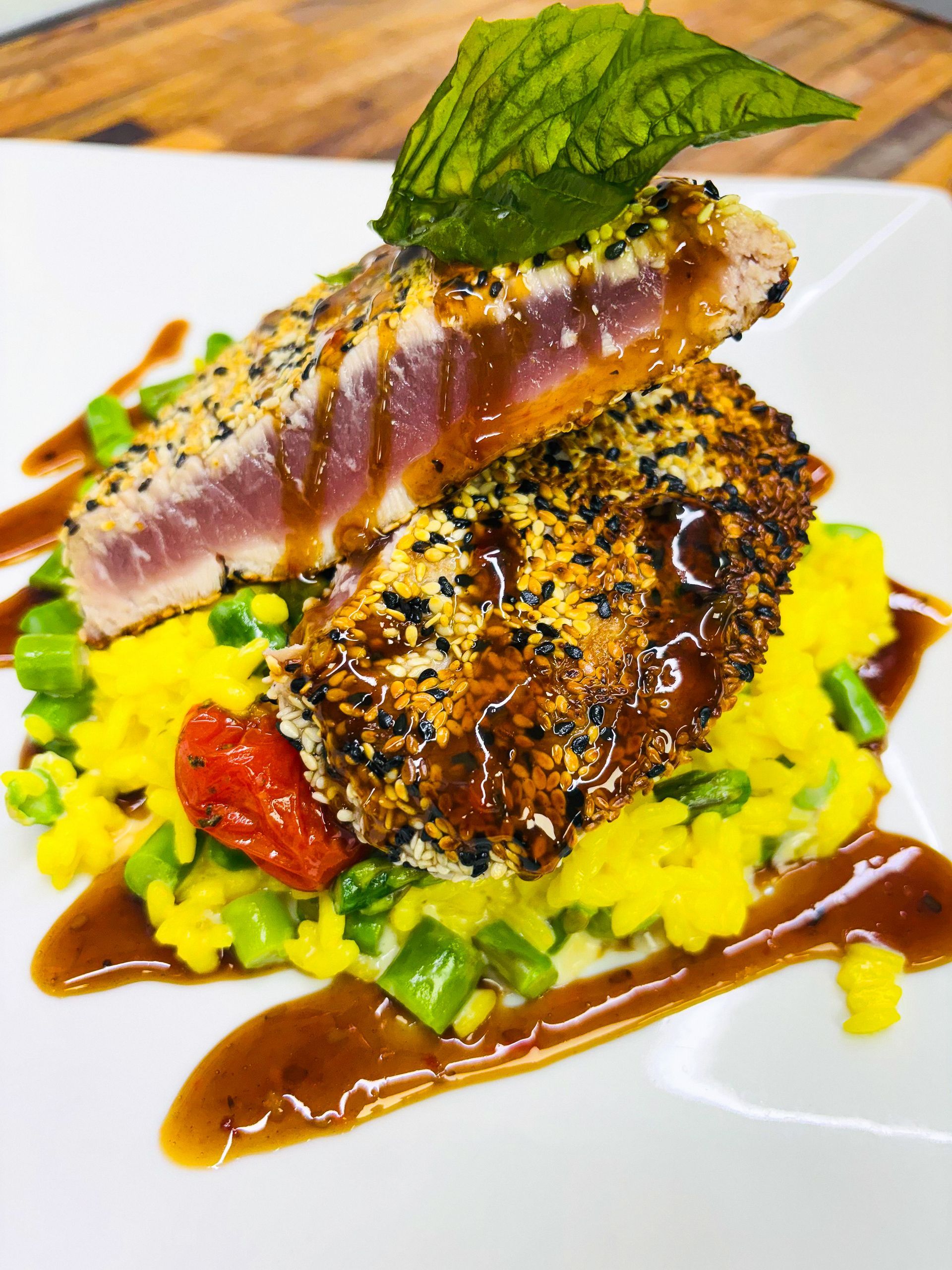Sesame-crusted tuna steak atop saffron risotto, drizzled with sauce and garnished with a mint leaf.