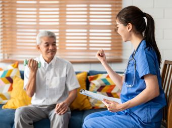 A nurse is talking to an elderly man while he exercises with a dumbbell.