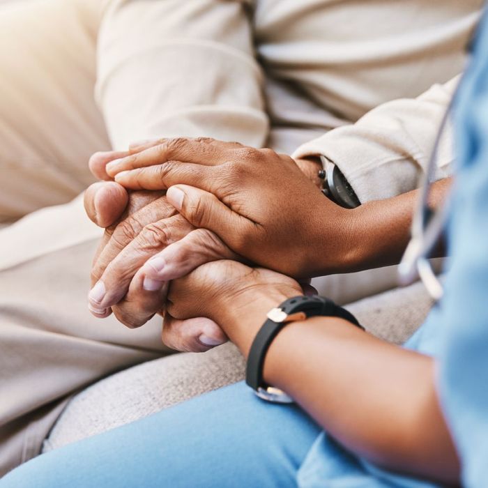 A nurse is holding a patient 's hands while sitting on a couch.