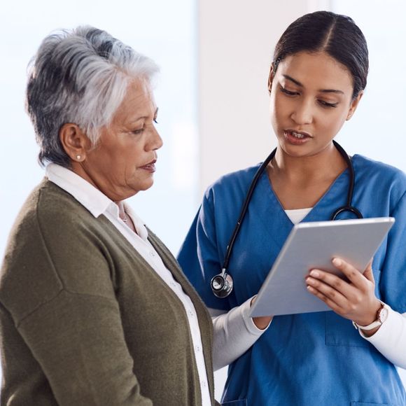 A nurse is looking at a tablet with an older woman.