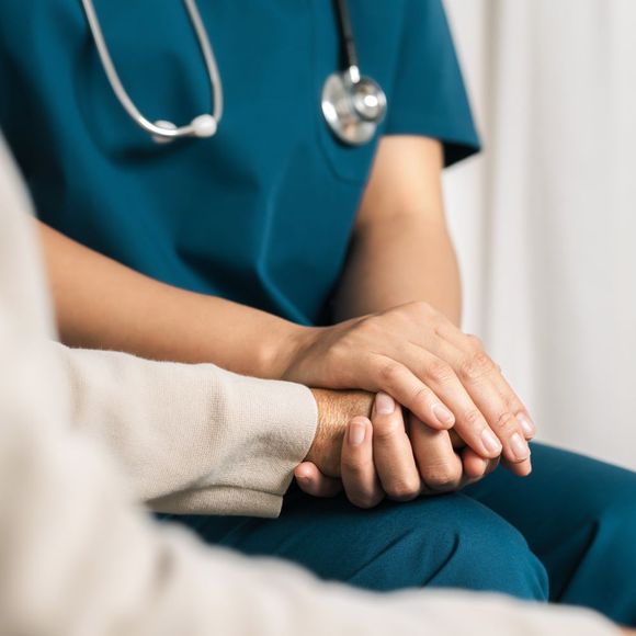 A nurse with a stethoscope around her neck is holding a patient 's hand